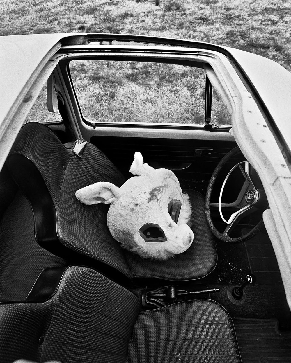 Black and white photo of vintage Volkswagen Beetle interior with a rabbit mask resting on the front passenger seat.