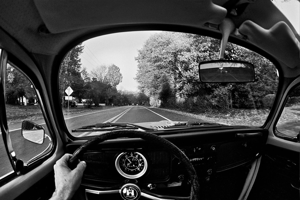 Black and white wide angle shot of a 1302 Super Beetle dashboard while driving down the road.
