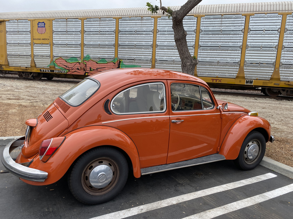 Orange Volkswagen Beetle parked beside a yellow freight train car.