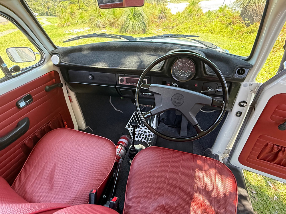 Right-hand-drive Volkswagen Super Beetle interior with red upholstery and period-correct dashboard