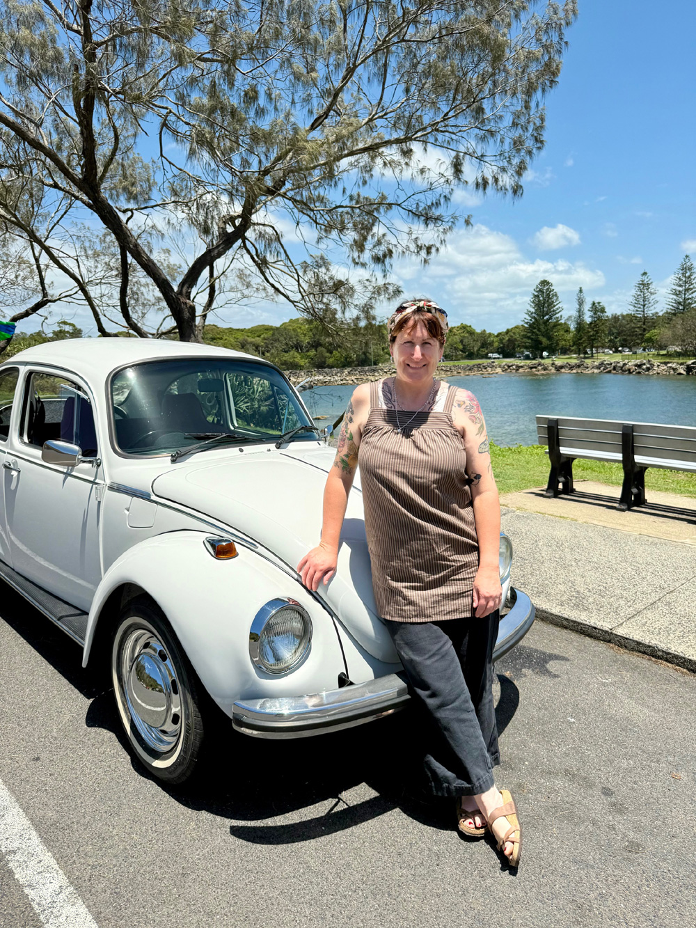 Owner standing beside his/her white Volkswagen Super Beetle near a waterfront park on a sunny day