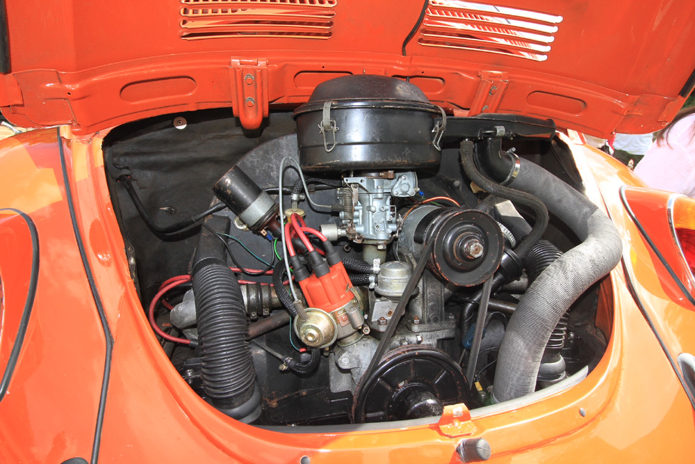 Air-cooled VW Super Beetle engine showing carburetor, distributor, and orange bodywork