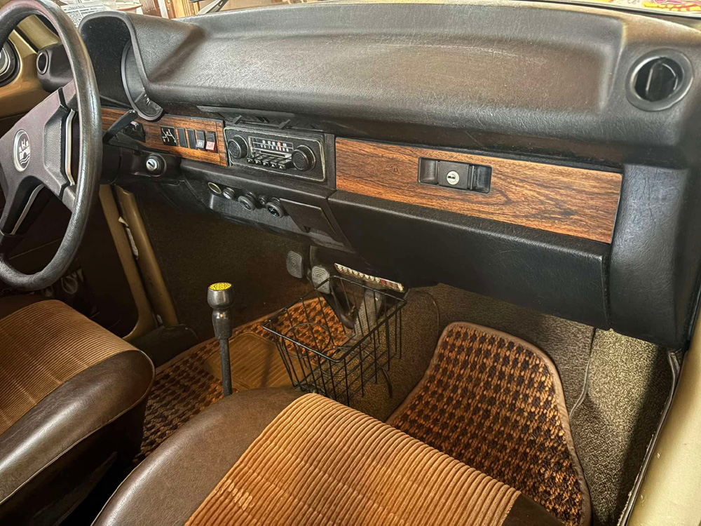 Vintage Beetle interior with woodgrain dashboard, classic radio, brown and tan striped seats, and floor mats.