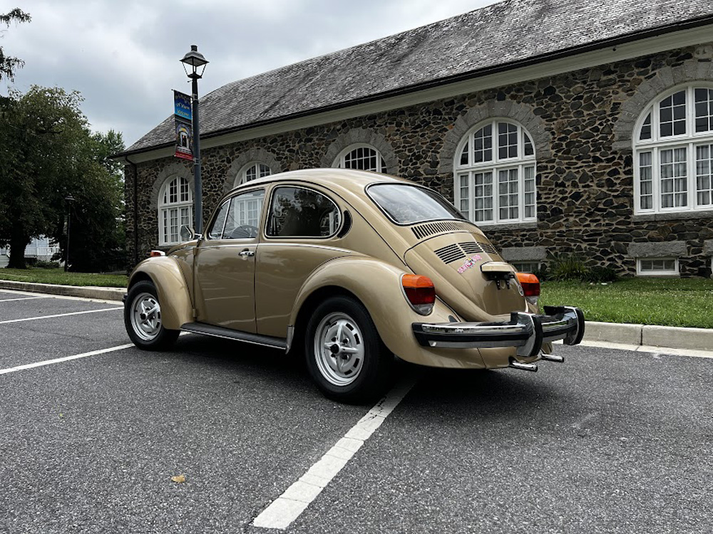 Gold Volkswagen Beetle parked in front of a historic stone building with arched windows and a lamppost.