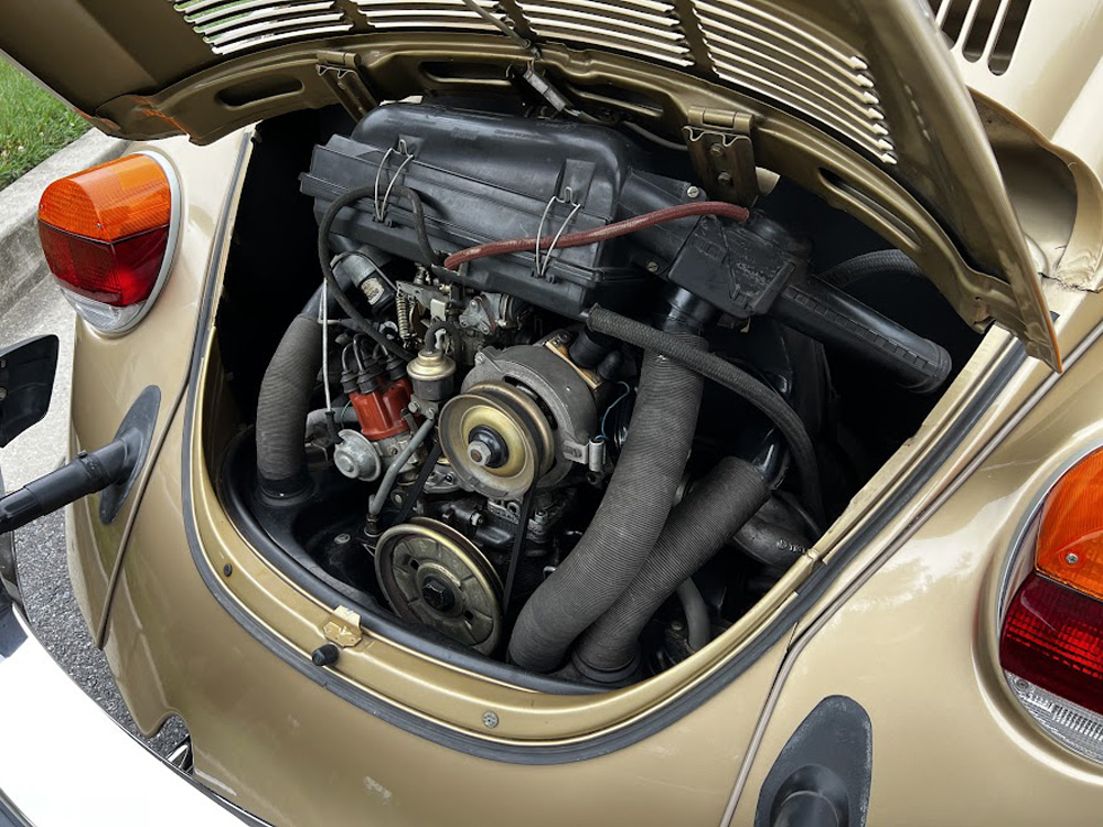 Rear engine compartment of a vintage Beetle showing the air-cooled flat four engine with fan shroud, carburetor, and ignition components.