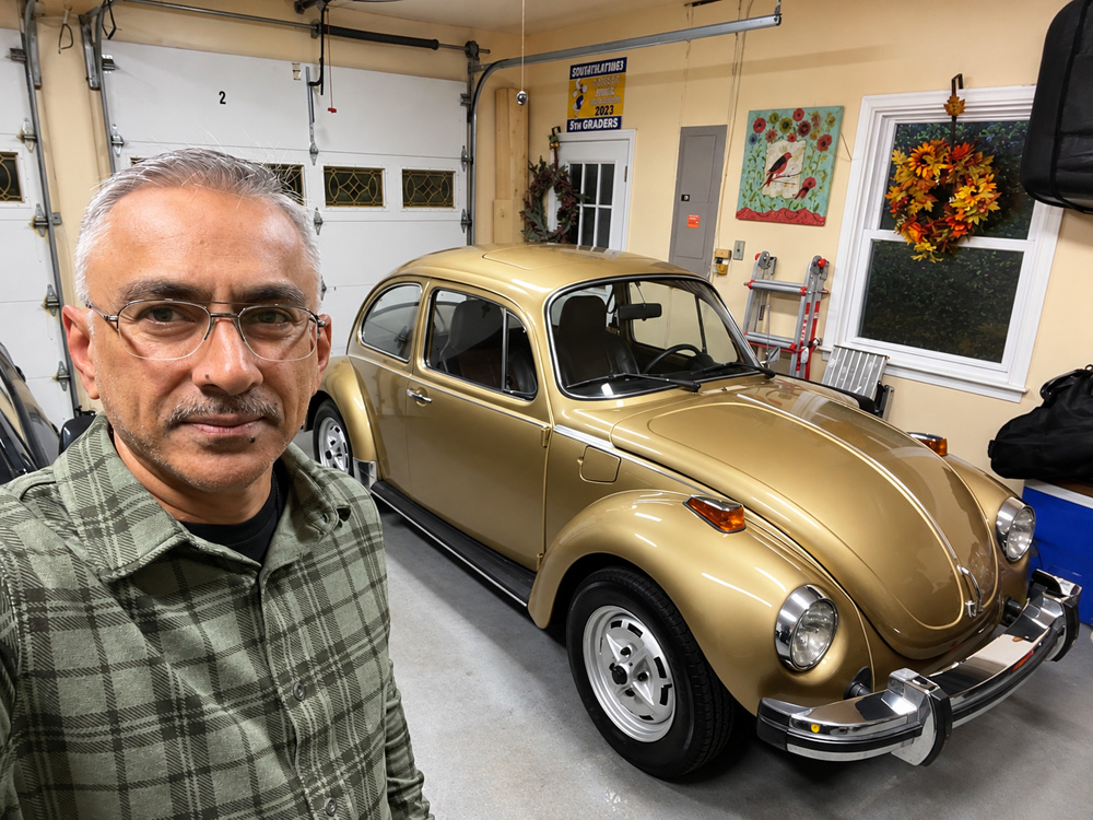 Ahmed Shah standing beside his gold Sun Bug inside a clean garage with fall decor and tools on the wall.