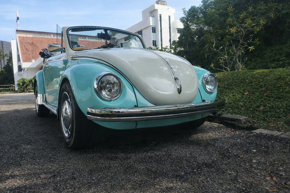 Turquoise and white Volkswagen Super Beetle convertible parked outdoors near a modern building
