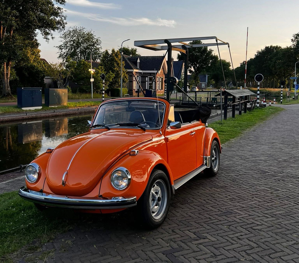 Orange Volkswagen Super Beetle convertible parked on a cobblestone street beside a canal