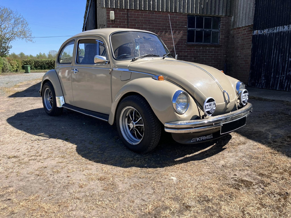Beige Volkswagen Super Beetle with Hella lights and Kamei front spoiler near a barn.
