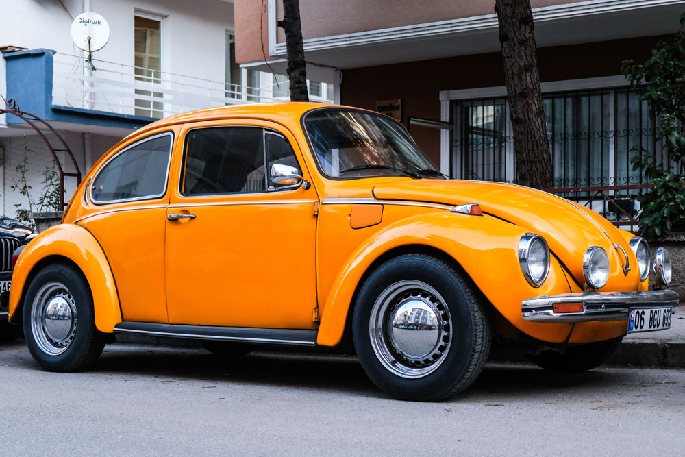 Yellow Volkswagen Super Beetle parked on a city street beside a residential building