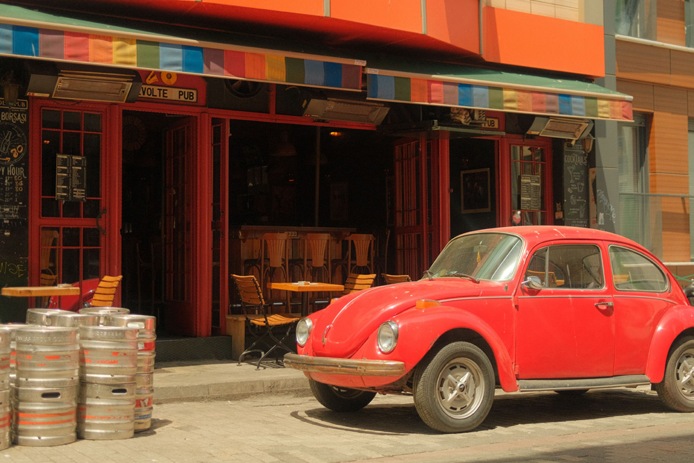 Red Volkswagen Super Beetle parked on a cobblestone street in front of a colorful pub