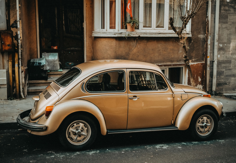 Beige Volkswagen Super Beetle parked on a narrow urban street beside an older building