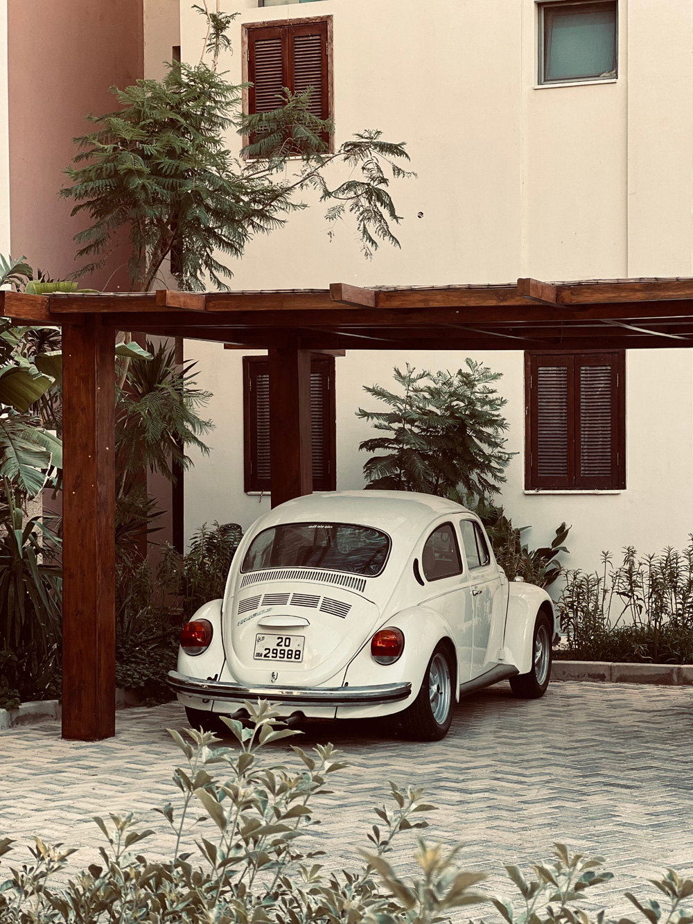 White Volkswagen Super Beetle parked under a wooden carport beside a modern residential building