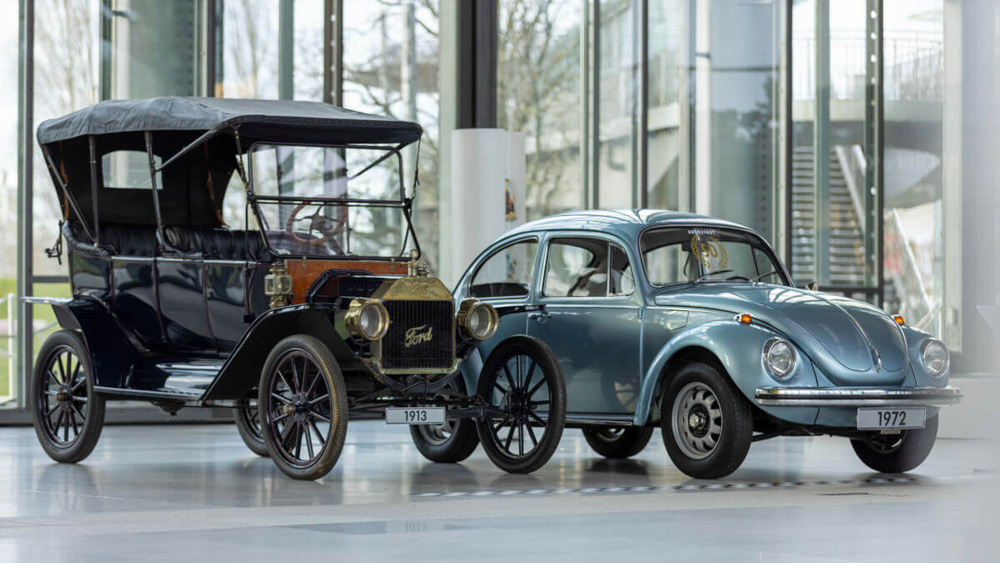 1913 Ford Model T and 1972 Volkswagen Marathon Beetle displayed side by side in a showroom for historical comparison