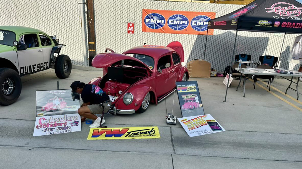 Pink Volkswagen Beetle display with VW Trends Magazine posters and a Dune Spec Beetle at the EMPI 70th Anniversary Open House