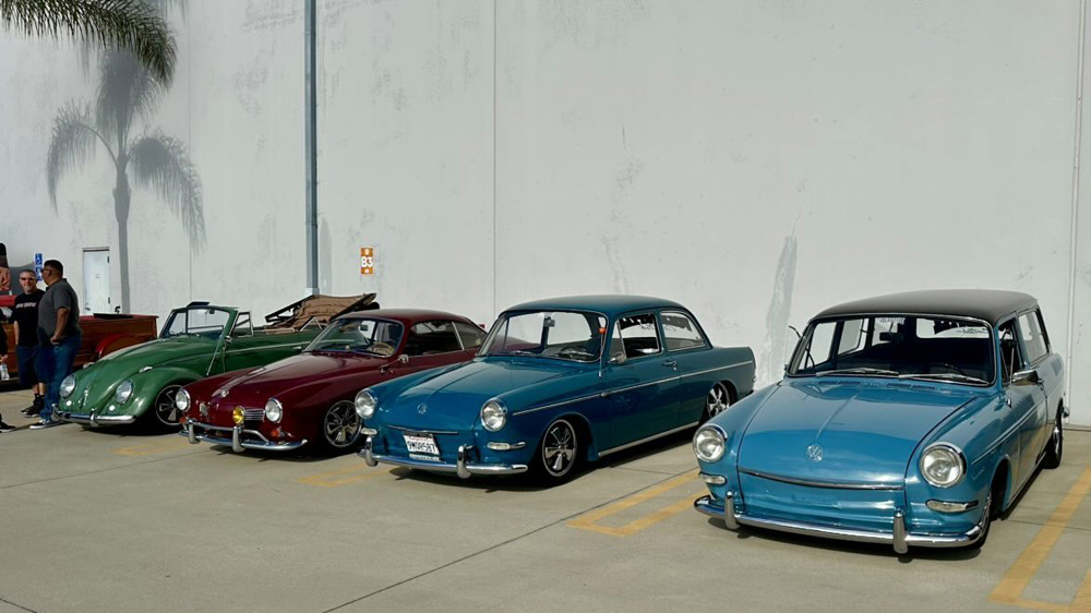 Green Beetle, maroon Karmann Ghia, teal Notchback and blue Squareback parked by a white wall at the EMPI 70th Anniversary Open House