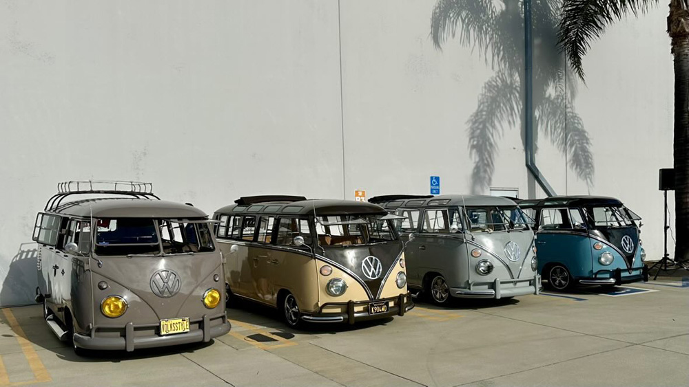 Four Volkswagen Buses in different colors parked side by side by a white wall at the EMPI 70th Anniversary Open House