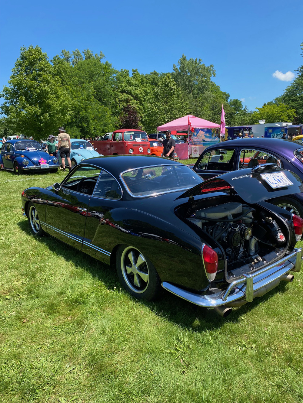 Black Karmann Ghia with open engine lid displayed among Beetles and a VW pickup