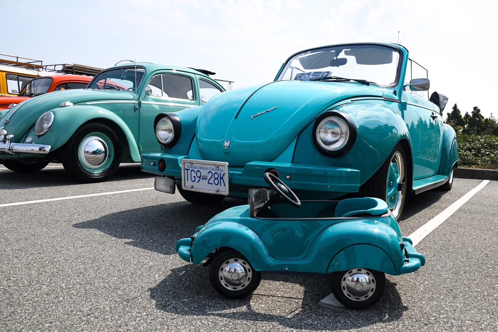 Turquoise Volkswagen Beetle convertible displayed with a matching miniature pedal car at the show