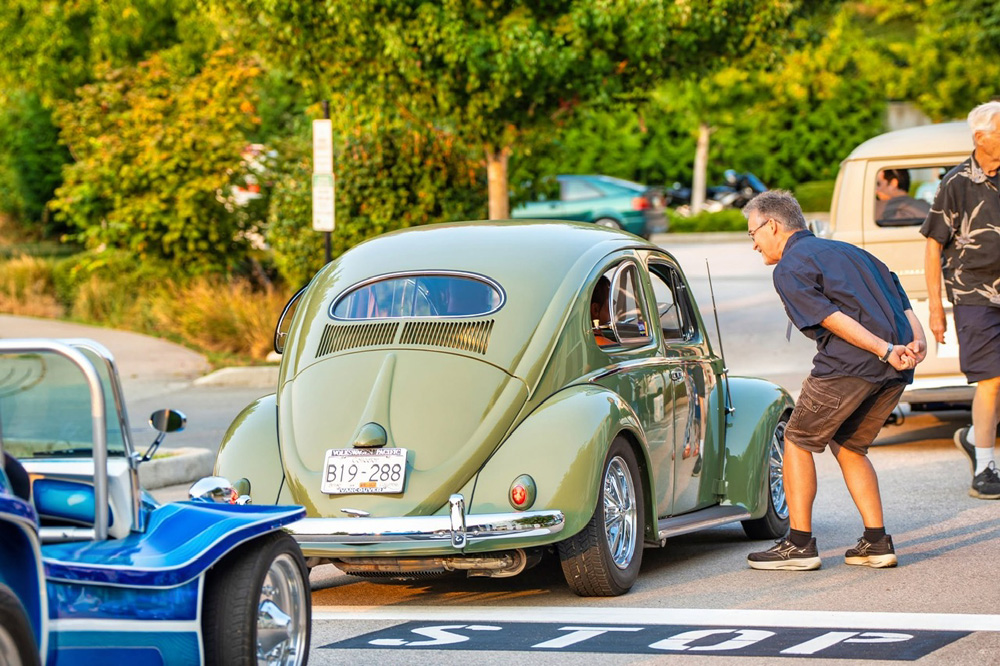 Light green vintage Volkswagen Beetle parked at a street meet with spectators looking closely at the car