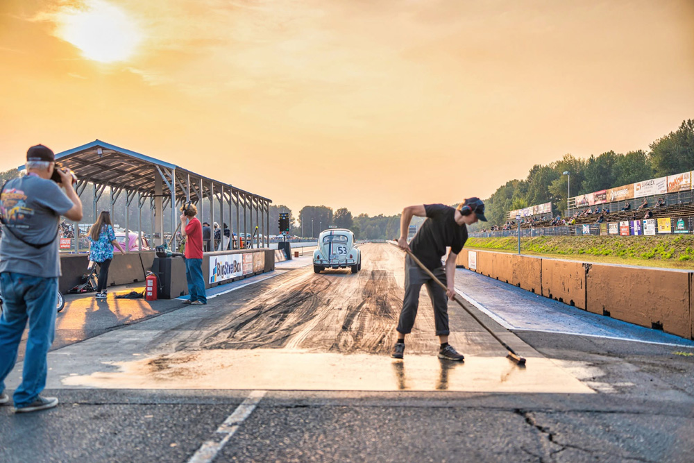 Track worker preparing the drag strip at sunset with a classic Volkswagen Beetle staged for racing